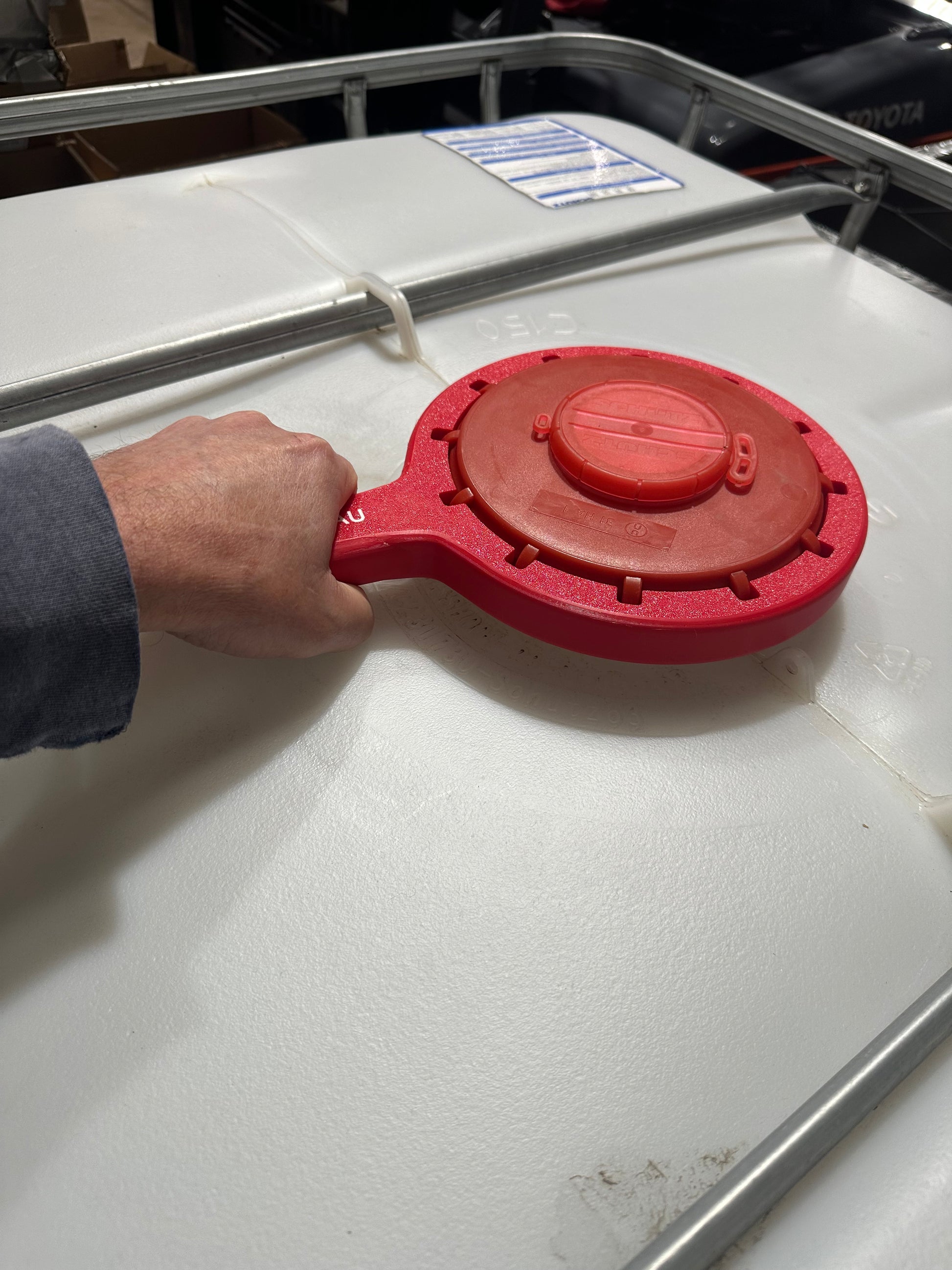 Hand using the Agimate IBC lid cap spanner to loosen the lid cap on an IBC tote.